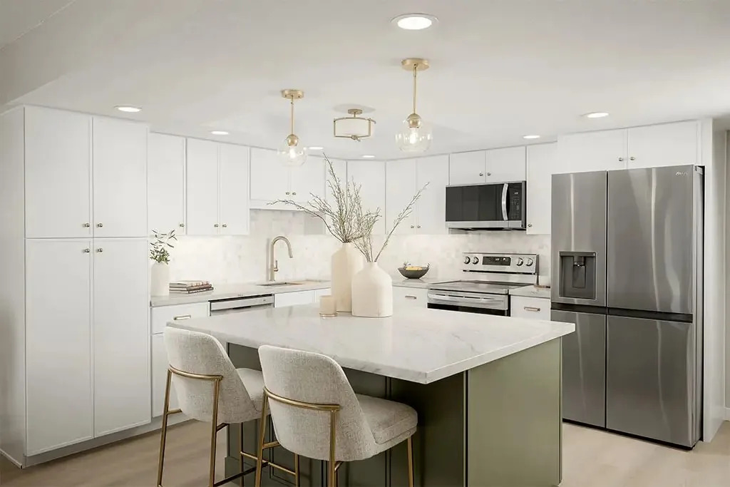 Remodeled white kitchen with a sage green island and brass pendants