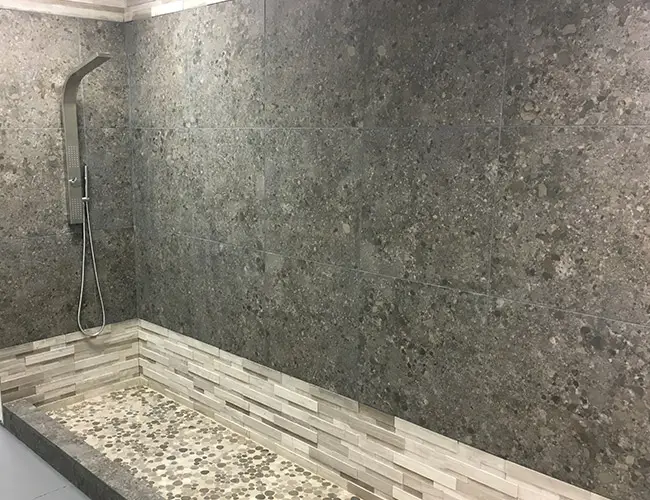 Walk-in shower with gray stone-look wall tile, a pebble floor and a low curb
