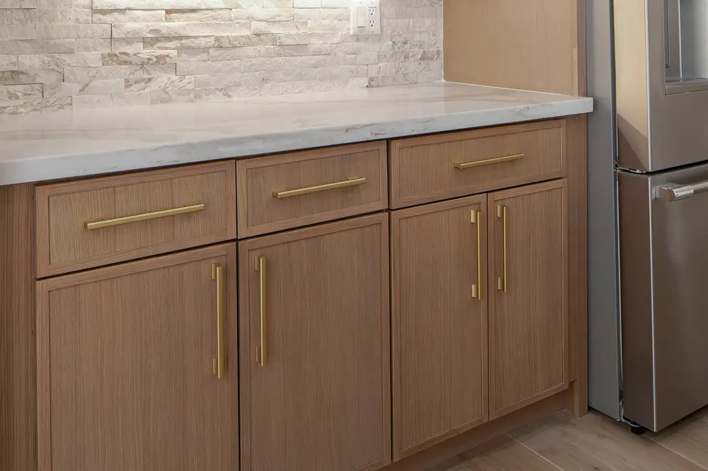 Wood cabinets with brass pulls and a stacked stone backsplash