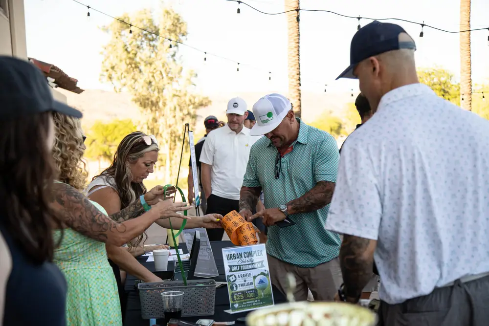 Tournament registration table with Urban Complex Charity Golf Tournament sign and Folds of Honor branding, participants purchasing raffle tickets