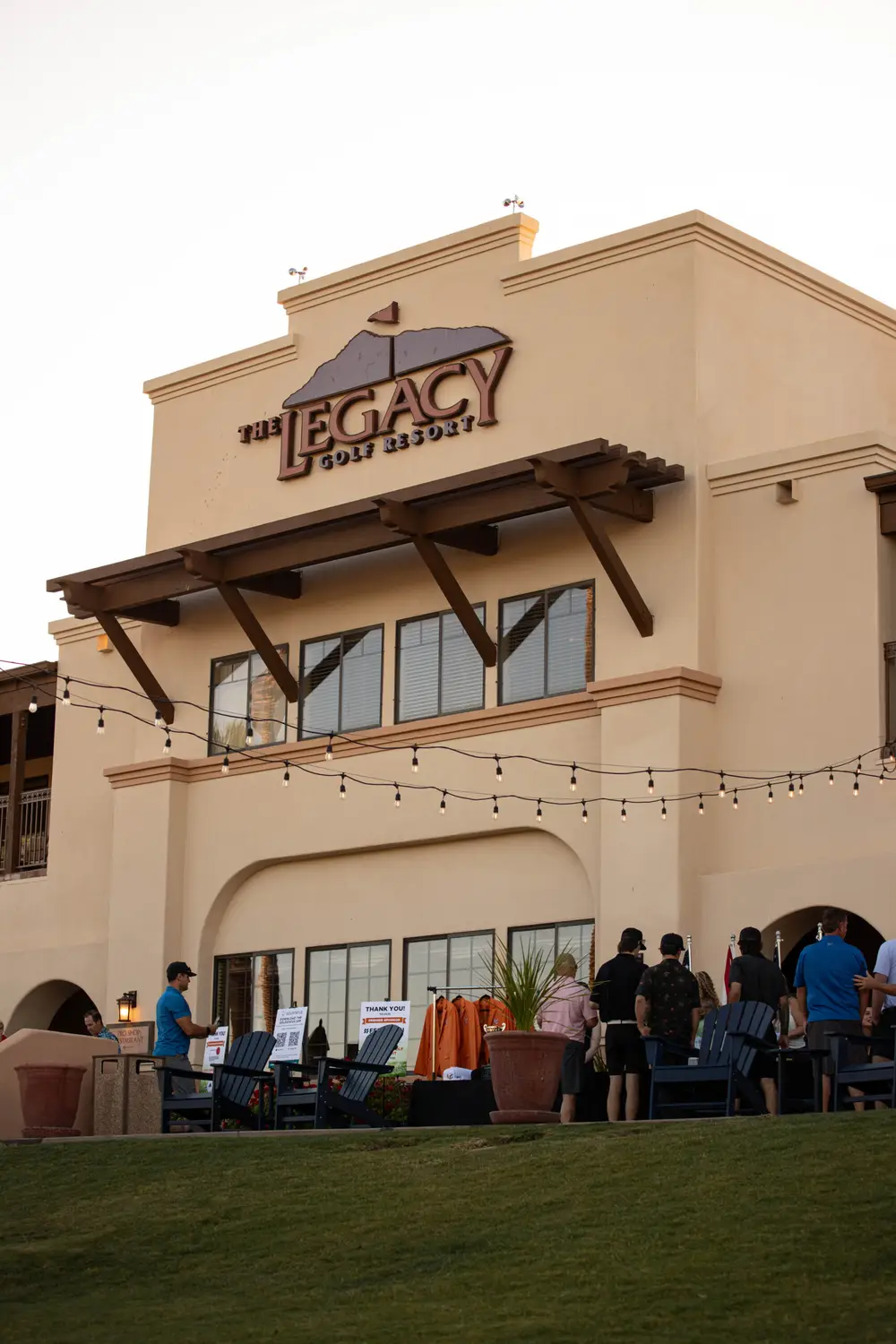 The Legacy Golf Resort clubhouse at dusk, with string lights and tournament attendees gathering on the patio