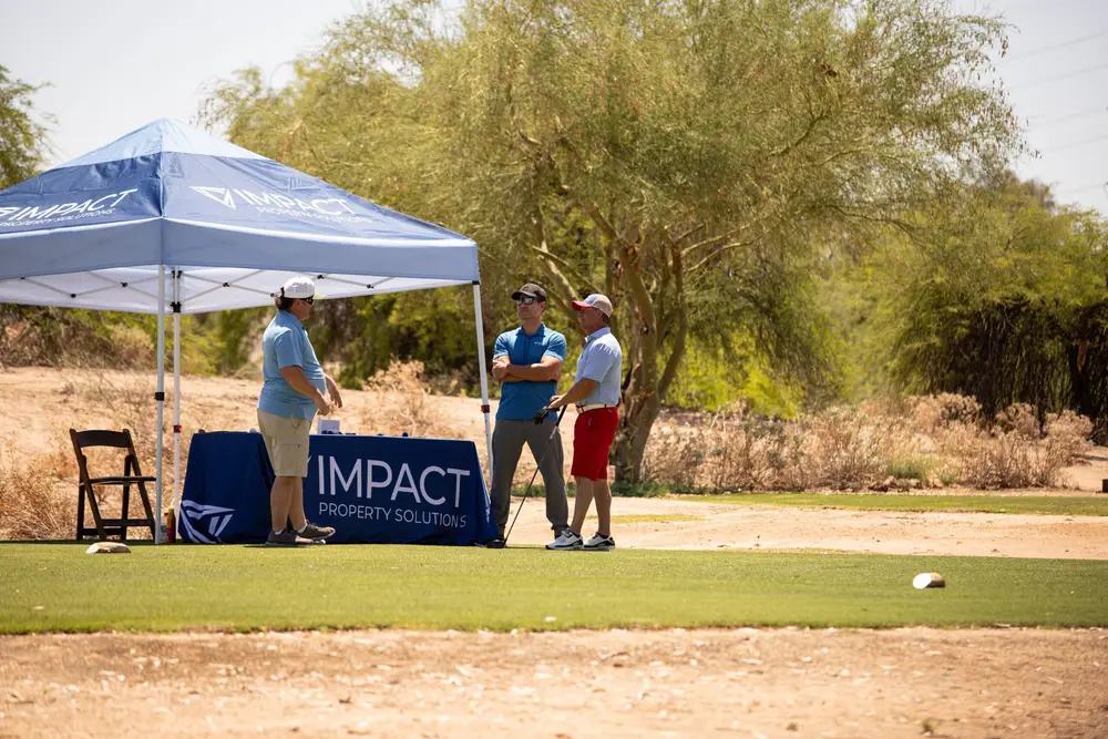 Golfers chatting with a hole sponsor representative under a branded tent on the sunny Phoenix course